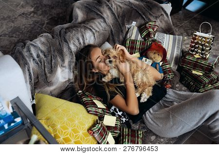 Tender Young Blonde Lying On A Couch, Kissing And Hugging Her Puppy. Tender And Warm Relations, Love