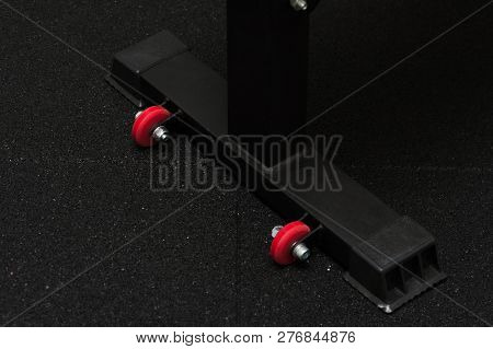 Close Up Of Rectangular Black Table Leg With Little Red Plastic Wheels On Black Dark Background. Two