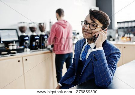Stylish Indian Business Man On Suit And Glasses Sitting At Cafe And Speaking On Phone.