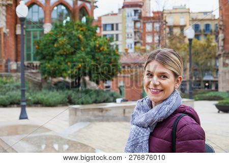Joyful Young Woman Wearing Prple Jacket And Grey Scarf Is Smiling To The Camera Outdoor