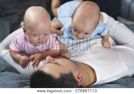 Young Father With His Newborn Twins Lying In Bed. Selective Focus