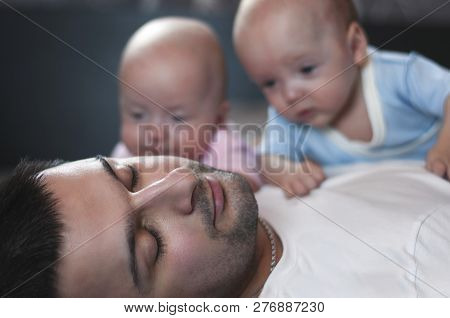 Young Father With His Newborn Twins Lying In Bed. Selective Focus