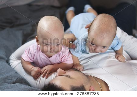 Young Father With His Newborn Twins Lying In Bed. Selective Focus