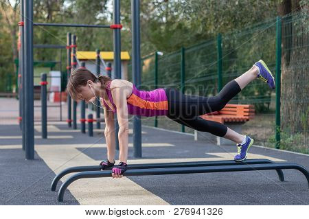 Young Caucasian Woman Workouts On The Park Sports Ground. In Sports Plank Position With One Leg Up, 