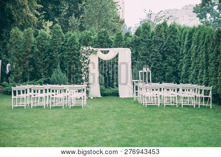 Beautiful Wedding Set Up. Area Of The Wedding Ceremony. Round Arch, White Chairs Decorated With Flow