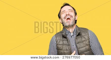 Middle age handsome man wearing winter vest Smiling and laughing hard out loud because funny crazy joke. Happy expression.