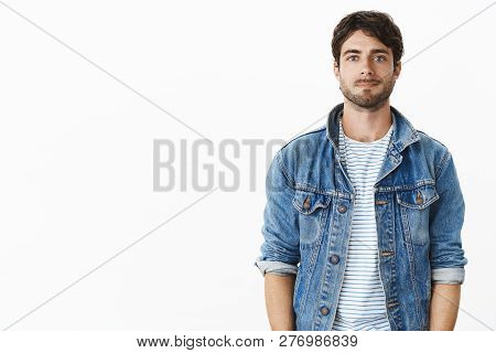 Waist-up Shot Of Nice Handsome Guy In Stylish Denim Jacket Over Striped T-shirt Smirking Shy And Awk