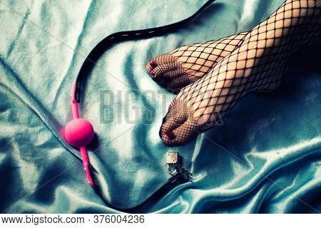Pink Gag Ball Lies On A Blue Satin Next To The Beautiful Female Legs In Stockings In A Fishnet. Bdsm