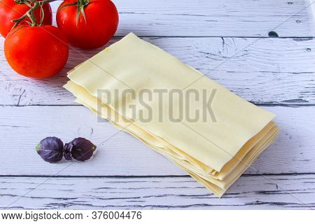 Lasagne Sheets Pasta With Tomato And Basil Leaf On A Wooden Background. Ingredients For An Italian R