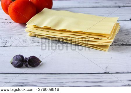 Lasagne Sheets Pasta With Tomato And Basil Leaf On A Wooden Background. Ingredients For An Italian R