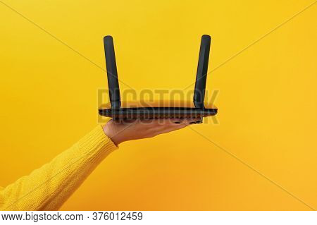 Black Wifi Router On Female Hand Over Yellow Background