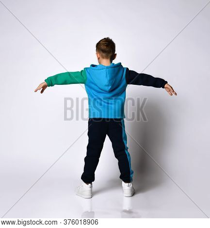 Rear View Of Little Boy Model In Fashionable Cotton Sportsuit Posing Doing Exercises Spreading Arms 