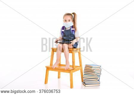 First-grader In Medical Mask Learns To Read. Little Girl On Home Distance Learning. Child In Medical
