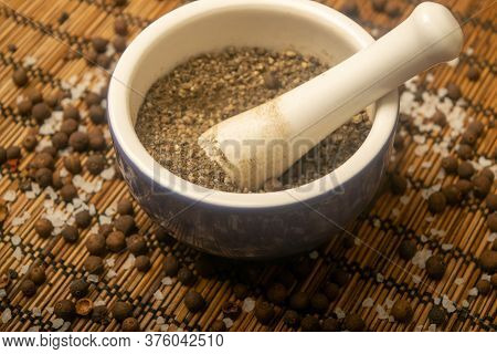 Ground Black In A Ceramic Mortar And Black And Coarse Salt Scattered On A Reed Mat. Close Up.