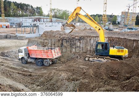 Crawler Excavator In Process Of Loading Sand Soil To Multi-ton Mining Truck At Construction Site Wit
