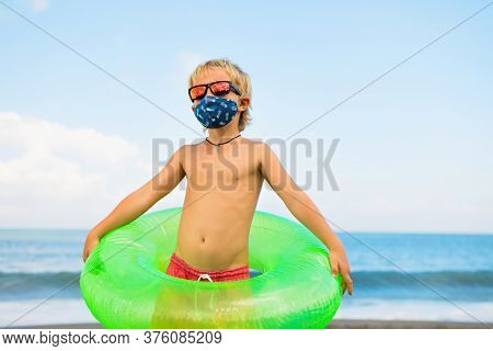 Funny Child In Sunglasses, Inflatable Ring On Tropical Sea Beach. New Rules To Wear Cloth Face Cover