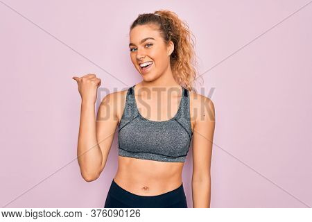 Young beautiful blonde sportswoman with blue eyes doing exercise wearing sportswear smiling with happy face looking and pointing to the side with thumb up.