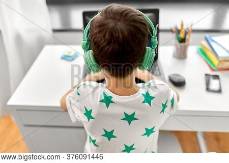 technology, gaming and people concept - boy in headphones playing video game on laptop computer at home
