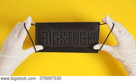 Two Hand With Latex Gloves And Black Face Mask On Yellow Background.