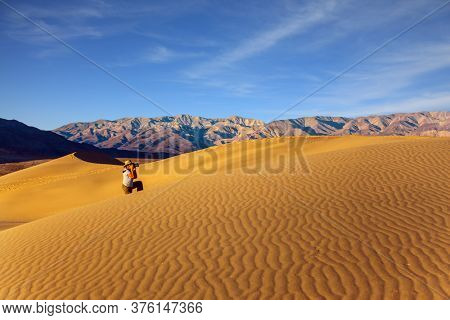 USA. Middle-aged woman photographs landscape. Mesquite Flat Sand Dunes is a part of Death Valley in California. Light sand waves from the desert wind. Concept of active, ecological and photo tourism