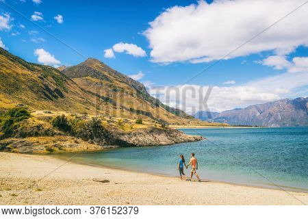 New Zealand travel people tourists visiting Otago region walking on shore of lake Hawea nature landscape. Man and woman happy at beach Near Wanaka. Young tramping hikers adventure lifestyle.