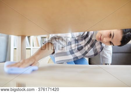 Young Housewife Using Rag To Wipe The Dust Under The Table In The Room At Home She Doing Chores