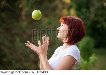 Beautiful Woman With Red Hair Catching Big Green Apple Falling From Above Outdoors. Cheerful Woman T