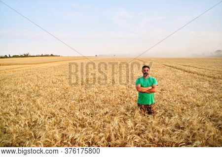 Happy Farmer Proudly Standing In Wheat Field With Arms Crossed On Chest. Agronomist Wearing Corporat
