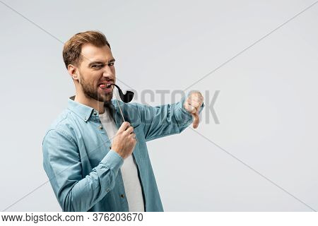 Funny Young Man With Fake Tobacco Pipe Showing Thumb Down Isolated On Grey