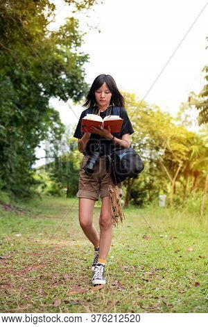 The Beautiful Woman Backpack And Holding Camera Around Neck,writing Travel Notes,walking In A Park ,