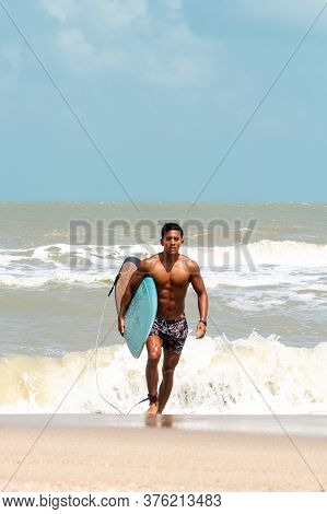 Young Handsome Man Wet All Over Body Holding Surfboard With Right Hand,walking On The Beach,show Fit