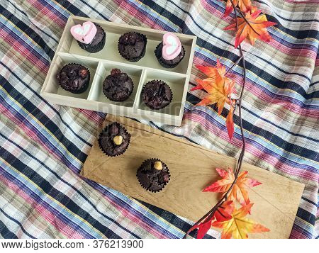 Top Vier Of Chocolate Cupcake And Magaroon Put Beside Dried Maple Leaf,on Colorful Table Cloth.