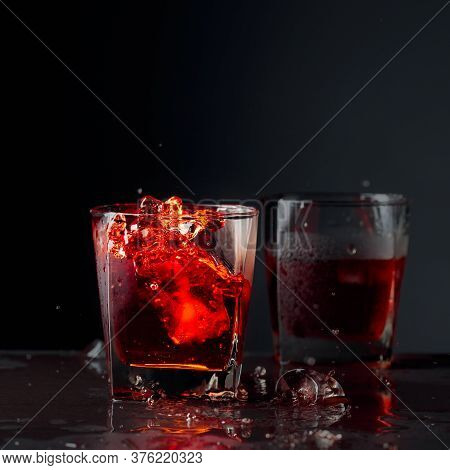 Pieces Of Ice Fall Into A Frosted Glass With Whiskey. Alcoholic Drink With Natural Ice On A Black Ba