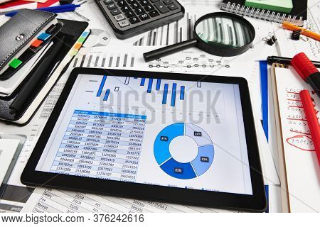 Top view of office employee's desk - work with tablet pc computer and financial reports, analysis and accounting, tables and graphs, various office items for bookkeeping