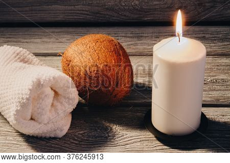 White Rolled Towel With Coconut And Burning Candle On Wooden Table. Spa Relaxtion Procedure.
