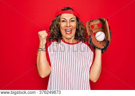 Middle age senior woman wearing baseball equiment, ball and glove over red isolated background screaming proud and celebrating victory and success very excited, cheering emotion