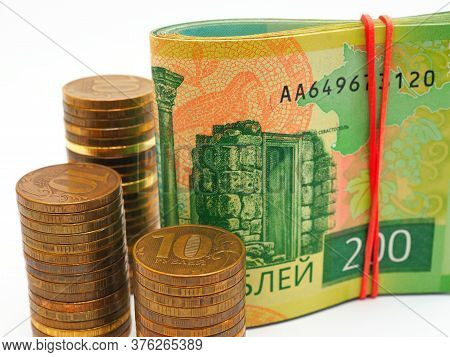 Piles Of Russian Coins Of 10 Rubles Stand Next To A Bundle Of Notes Of 200 Rubles. Contrast And Satu