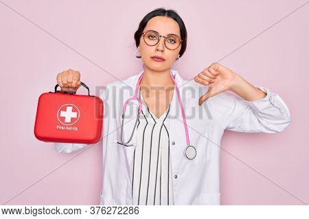 Young beautiful doctor woman with blue eyes wearing stethoscope holding first aid kit box with angry face, negative sign showing dislike with thumbs down, rejection concept