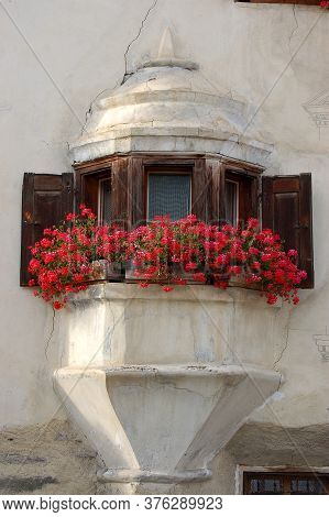 Old Balcony With Wooden Windows And Red Geraniums In The Ancient Village Of Guarda, Scuol Municipali