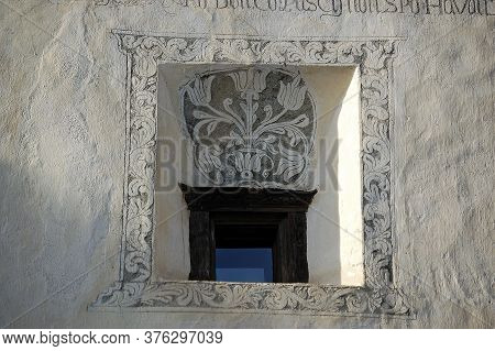 Small Old Window With Floral Decorations On White Wall In The Ancient Village Of Guarda, Scuol Munic