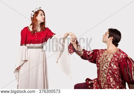Young man in old-fashioned costumes holding princess's hand against gray background