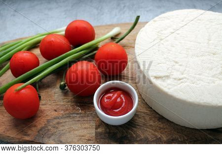 Homemade cheese made from goats milk, small tomatoes on a branch, red sauce lie on a wooden Board on
