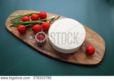 Homemade Goats Milk Cheese, Small Tomatoes On A Branch, Red Sauce On A Wooden Board On A Dark Green 