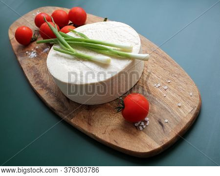Homemade Goats Milk Cheese, Small Tomatoes On A Branch, Red Sauce On A Wooden Board On A Dark Green 