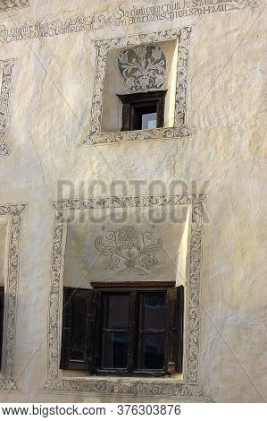 Two Old Windows With Floral Decorations On White Wall In The Ancient Village Of Guarda, Scuol Munici