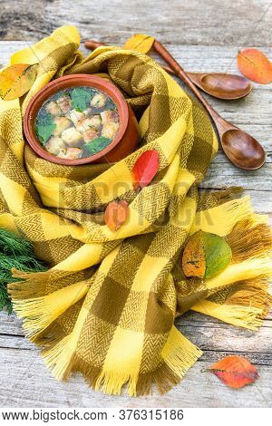 Soup With Croutons And Dill In A Clay Pot Wrapped In A Checkered Yellow Scarf For Warmth And Strewn 
