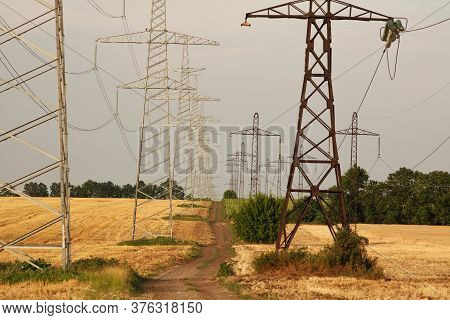 Dirt Country Road Between Fields Of Ripe Dry Wheat On A Background Of Metal Pylons Electrical Wires