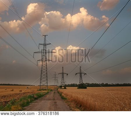 Dirt Country Road Between Fields Of Ripe Dry Wheat On A Background Of Metal Pylons Electrical Wires