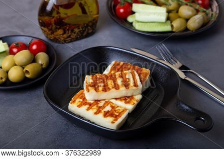 Grilled Haloumi Cheese On A Black Pan With Olives, Tomatoes, Cucumbers And Pepperoni. Close-up.