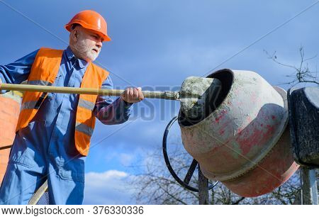 Construction Worker With Spade In Hand. Builder Works With Concrete Mixer. Concrete Mixer Prepares C